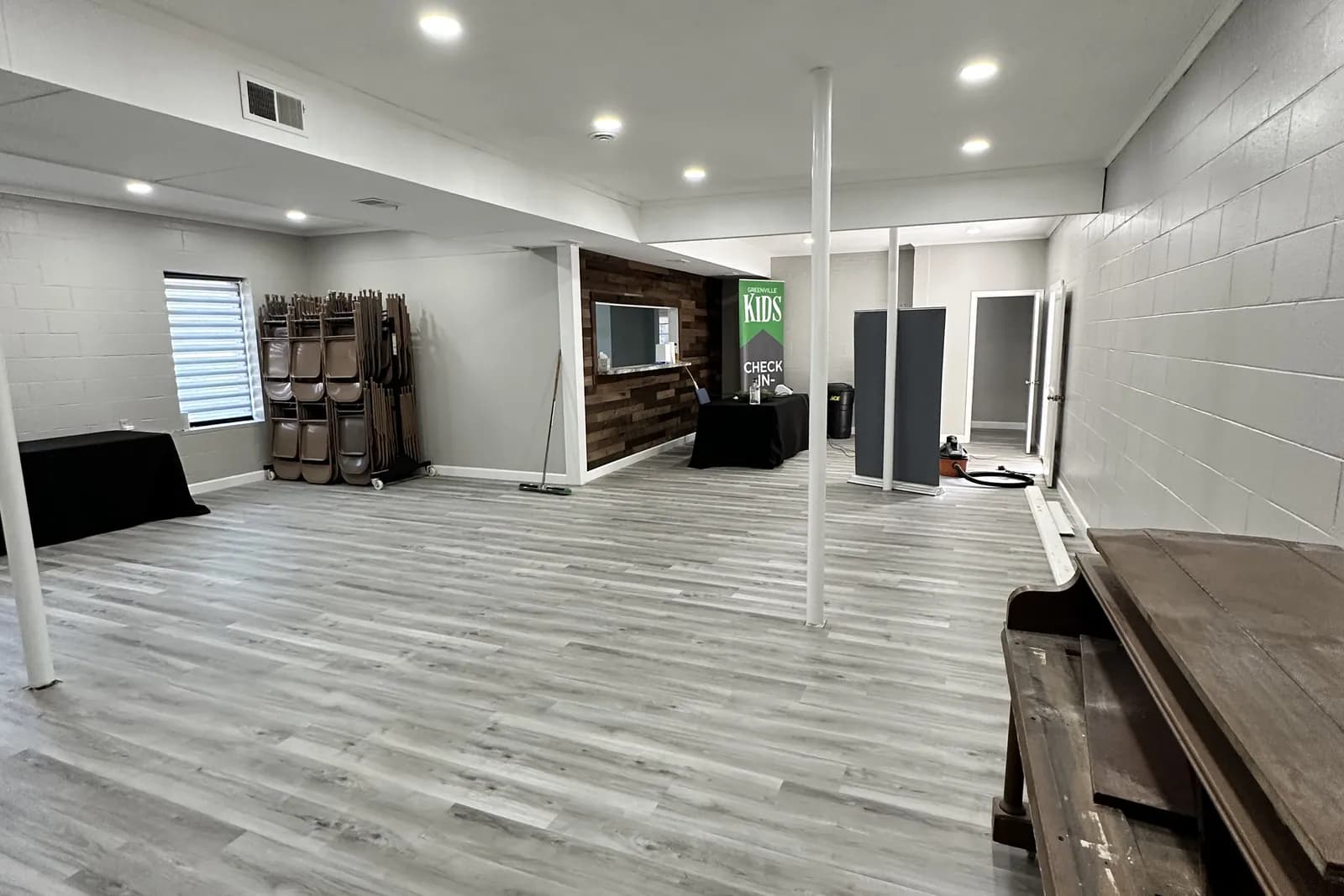 Renovated Greenville Community Church fellowship hall with new luxury-vinyl-plank flooring, a wood-accent feature wall, and a kids check-in area, completed by BHR Construction