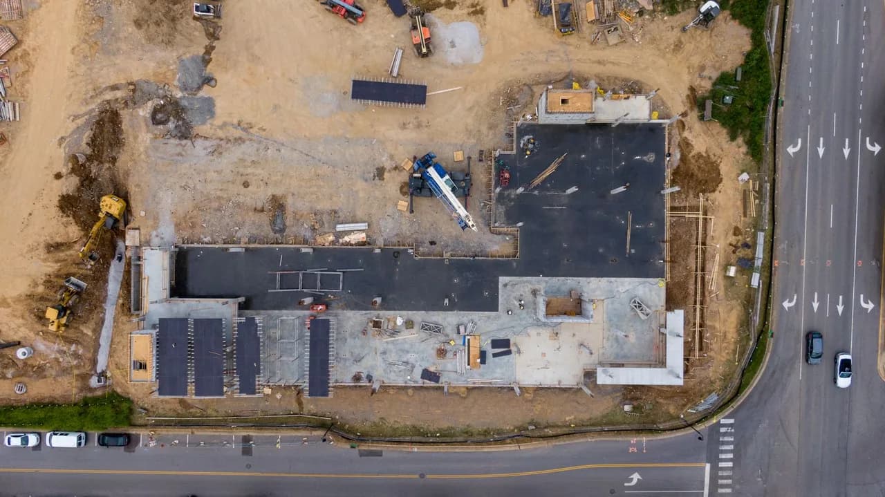 Aerial view of a commercial new-construction site with foundations, a crane, and active site work