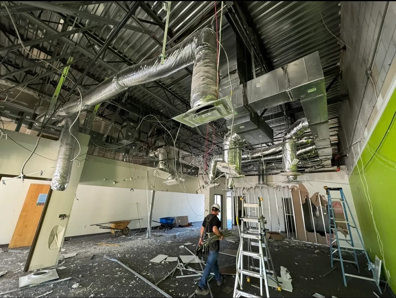 Commercial interior renovation in progress, showing exposed steel roof framing and new spiral HVAC ductwork being installed by BHR Construction