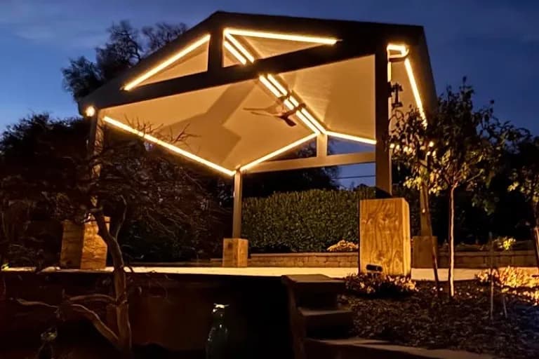 Peaked black-metal pergola with integrated LED lighting over an outdoor living and kitchen area